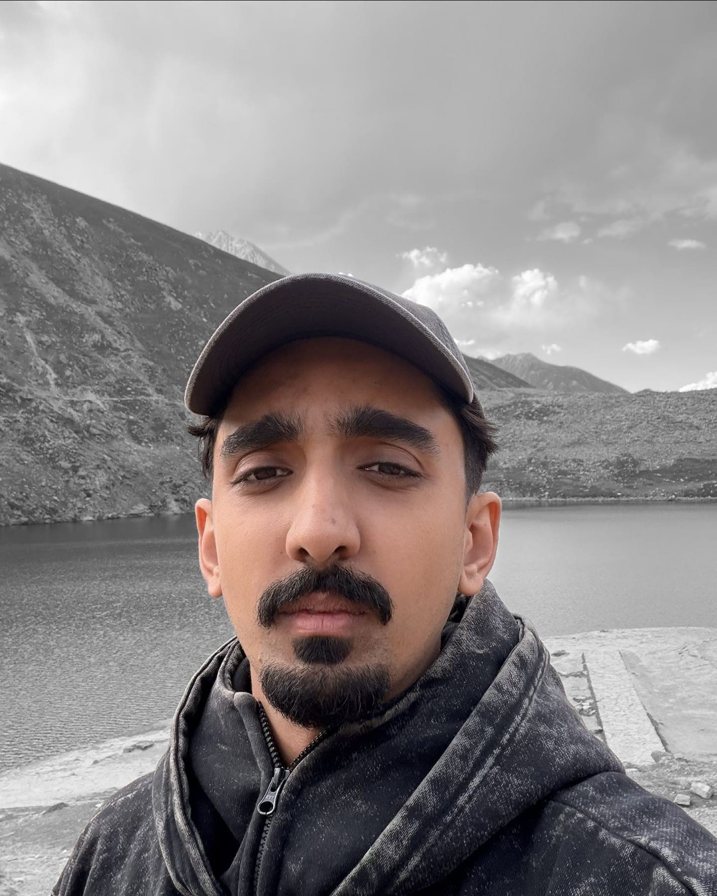 Sarib in a cap by a mountain lake, in black and white