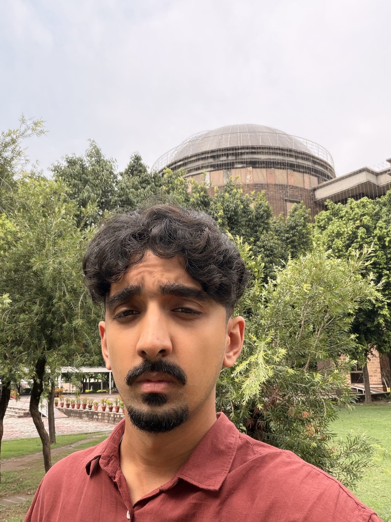 Sarib outdoors under green trees, a domed building behind him