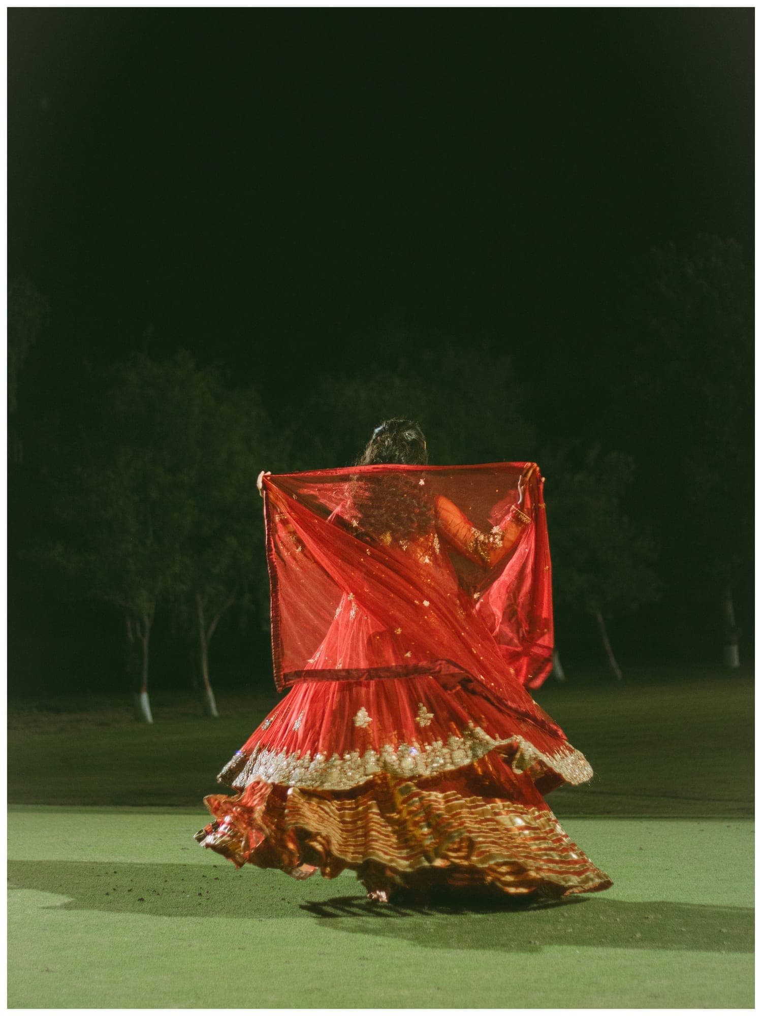 A dancer in a red dress spinning on grass at night
