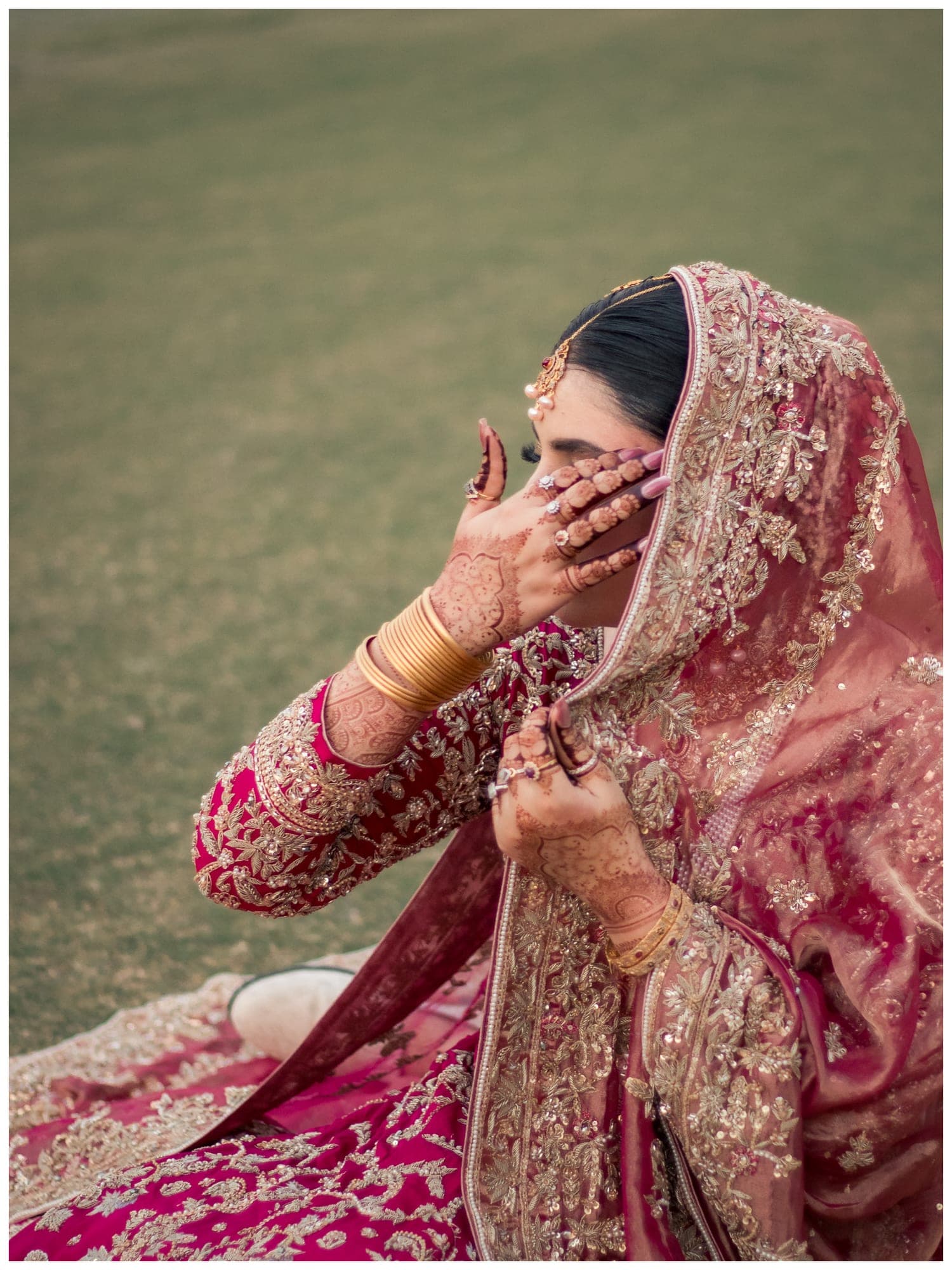 A bride in a red dupatta covering her face with hennaed hands